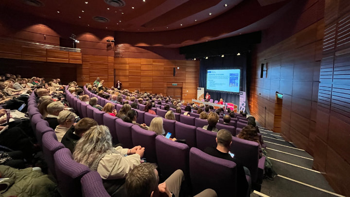 A photo from the back of a busy lecture theatre, with Kezia and Nicola presenting at the front