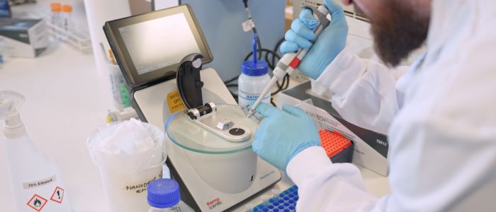Scientist using a pipette with laboratory equipment on a benchtop.
