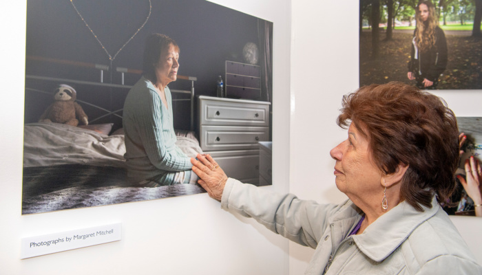A visitor views a mounted photograph showing a woman sitting on a bed