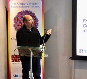 Prof David Bhella at a clear lecturn delivering a talk